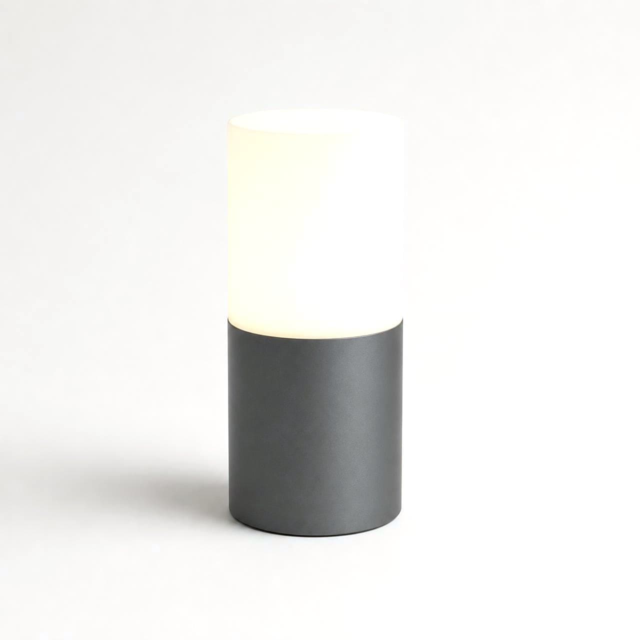 The Mirrorfolio Home Hub — a softly lit table lamp on a graphite base, sitting quietly in a room
